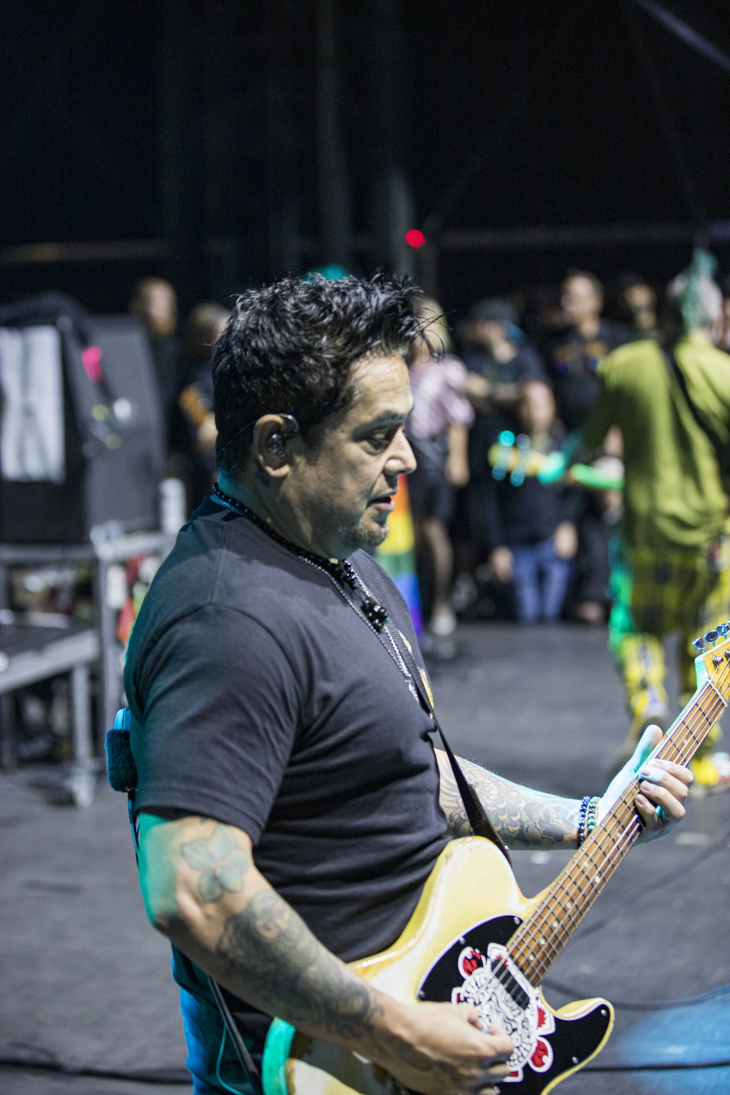 A man with tattoos and black hair playing an electric guitar on stage during a concert.