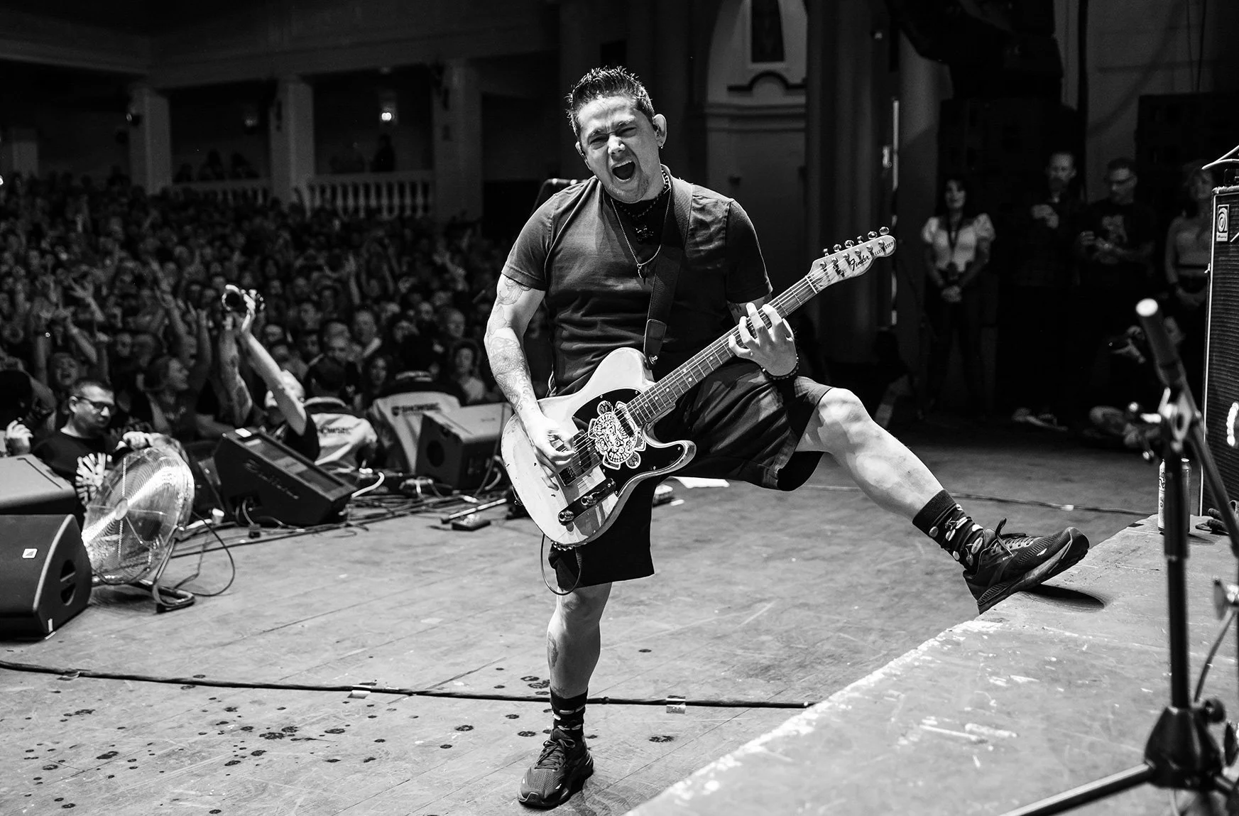 A musician passionately performs on stage with a guitar in front of a large crowd, black and white photo.