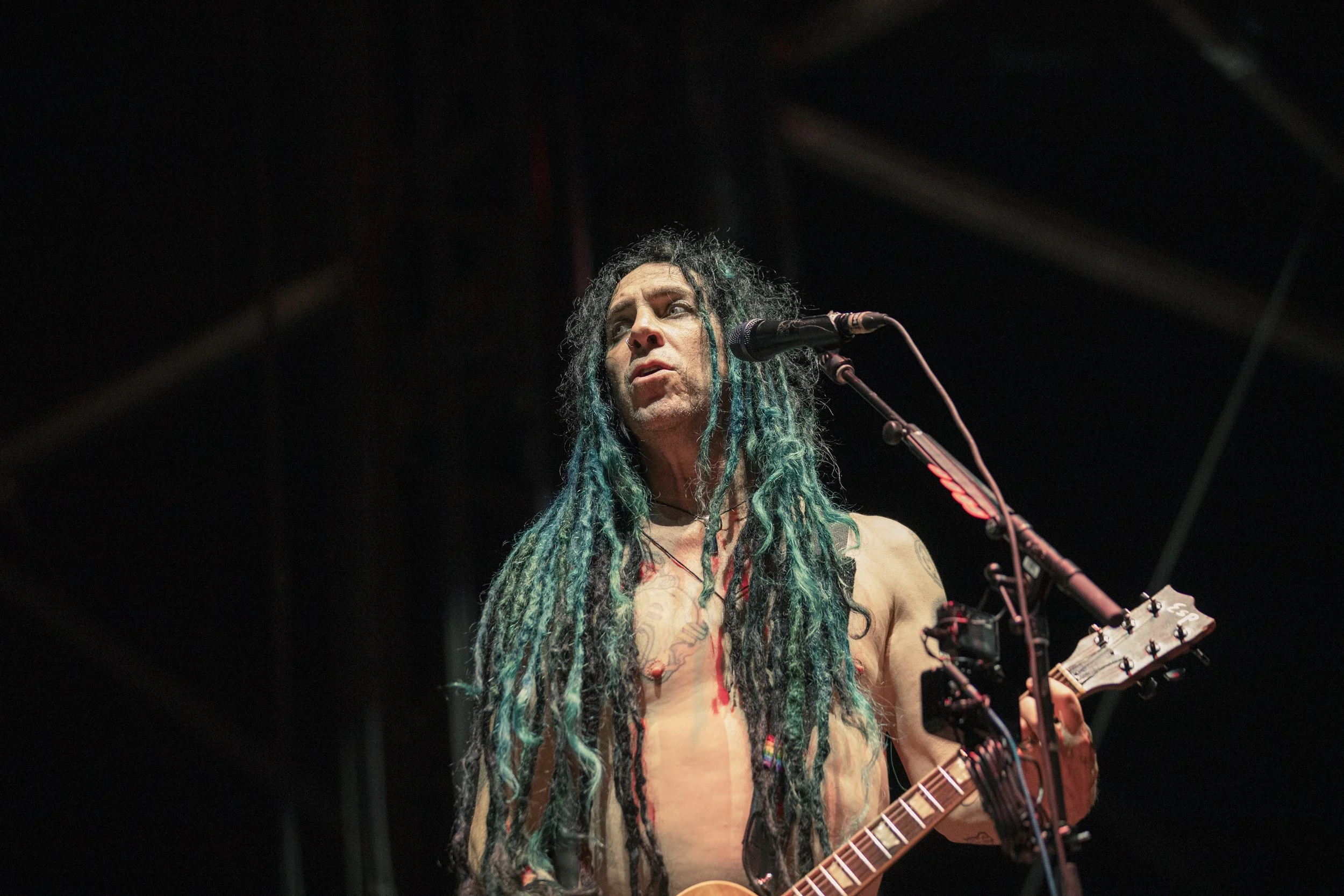 Shirtless man with long dreadlocks playing guitar on stage.