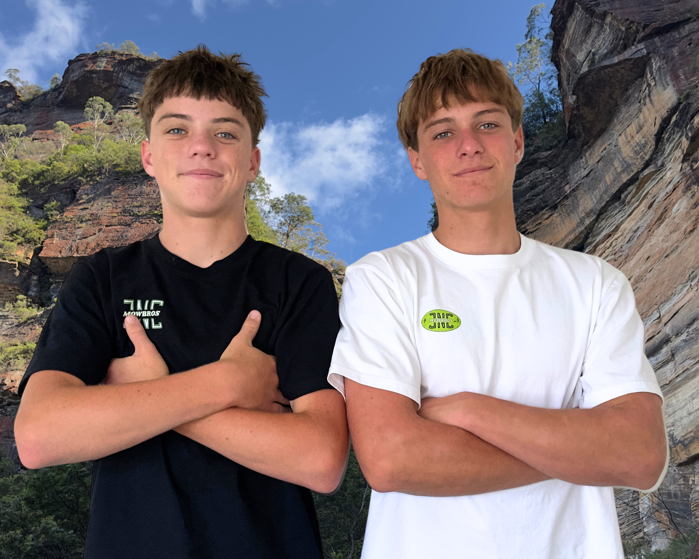 Two teenage boys standing side by side with arms crossed in front of a scenic rocky outdoor background with trees and blue sky.