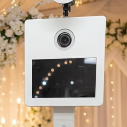 Eine weiße Premium Fotobox mit großem Bildschirm in einer festlichen Umgebung mit Blumen und Lichterdekorationen.