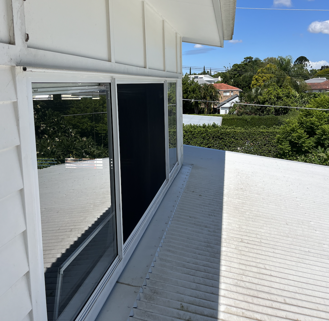 View from a balcony with sliding glass doors showing greenery and neighboring houses in a suburban neighborhood on a sunny day.
