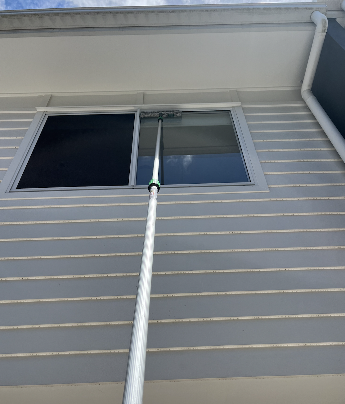 A person using a long roller to clean or paint the exterior wall of a building beneath a window.
