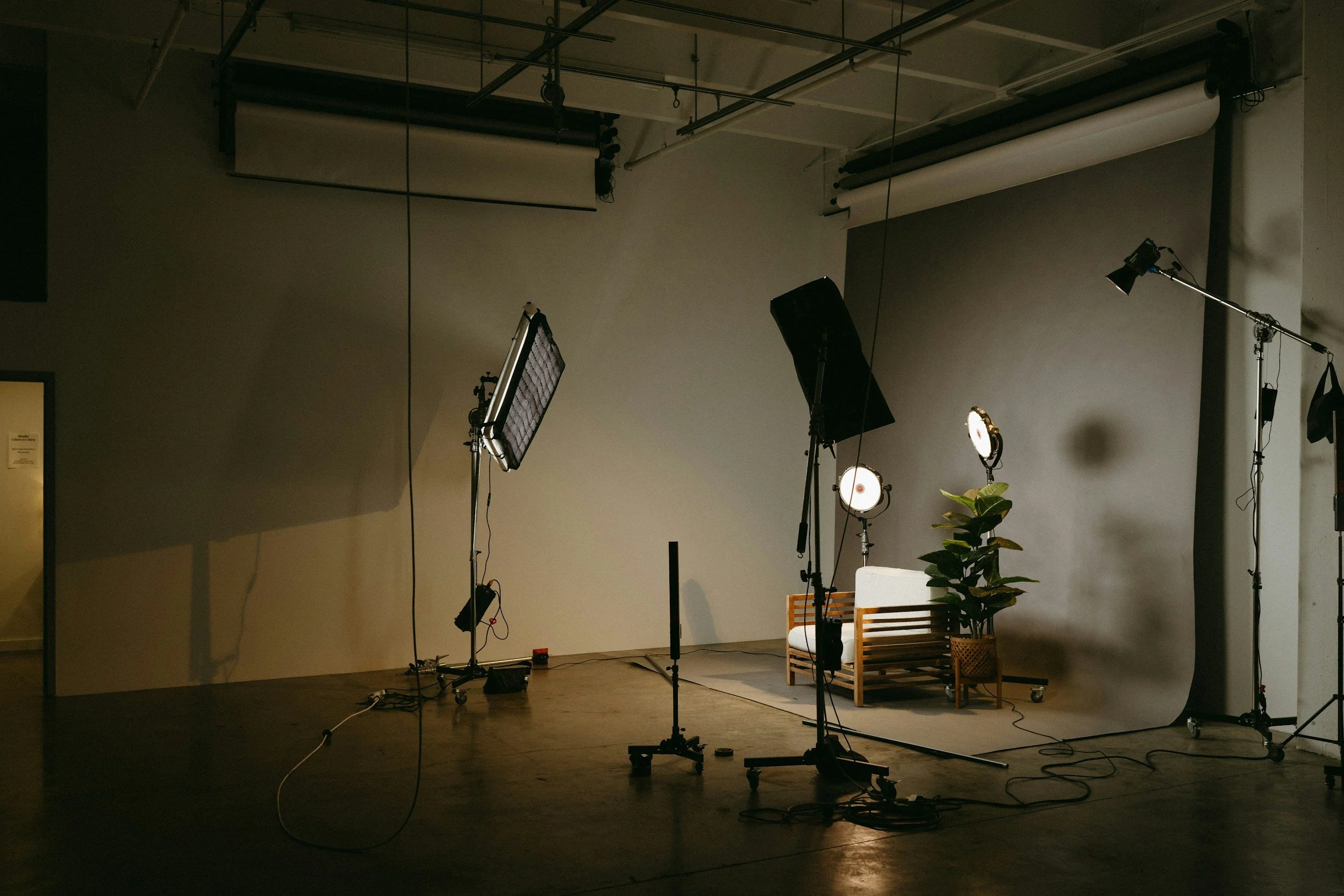 Photography studio with professional lighting equipment, a white bench, a potted plant, and a plain backdrop in a spacious room.