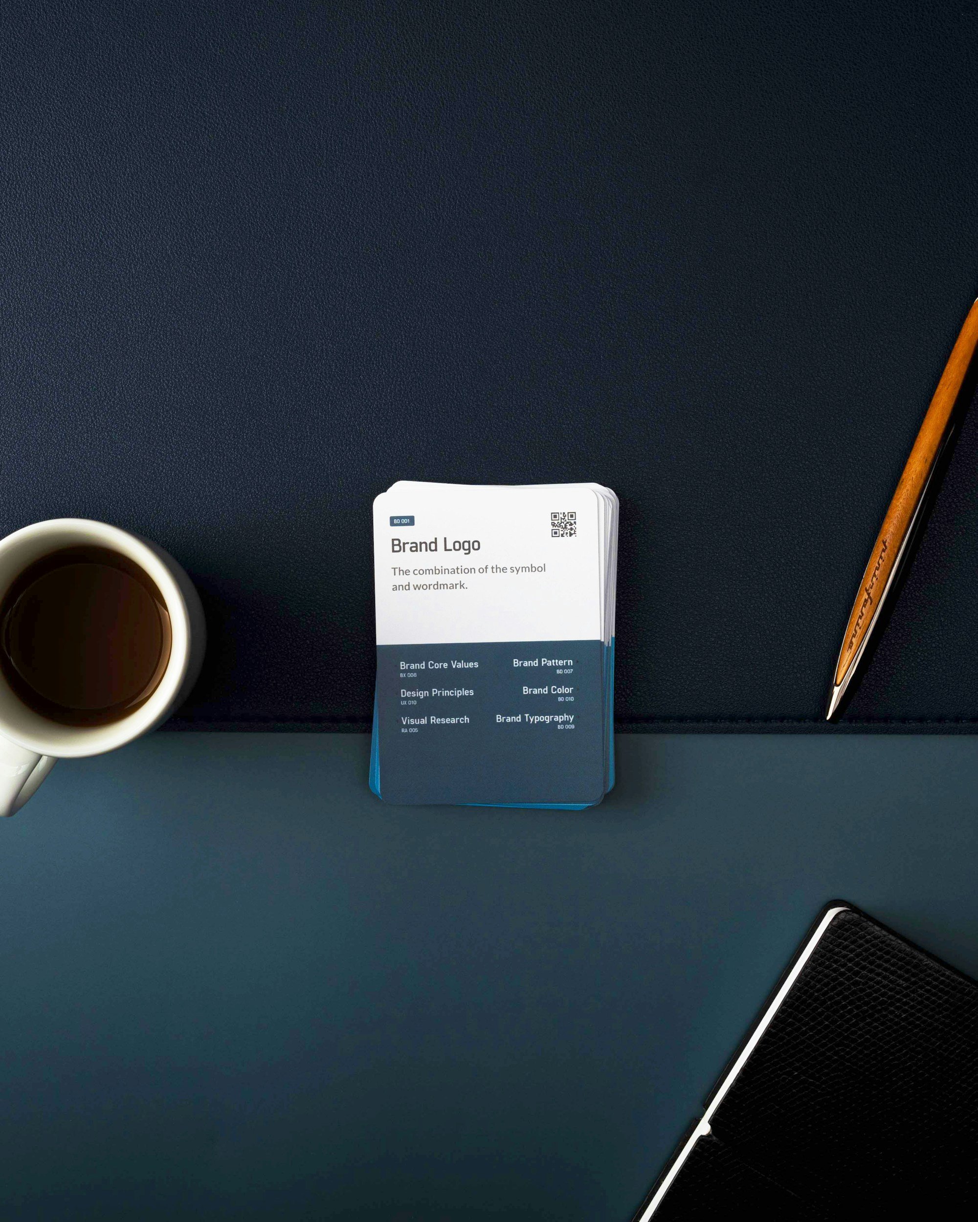 Desk scene with a white coffee mug filled with coffee on the left, a deck of brand branding cards in the center, and a pen and part of a closed laptop on the right.