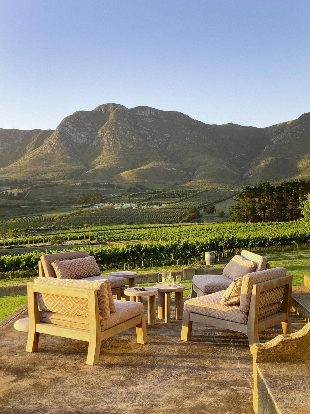 Outdoor seating area with four chairs and small tables, overlooking a vineyard and mountains. Private luxury villa (accommodation) in Hemel-en-Aarde, Hermanus.