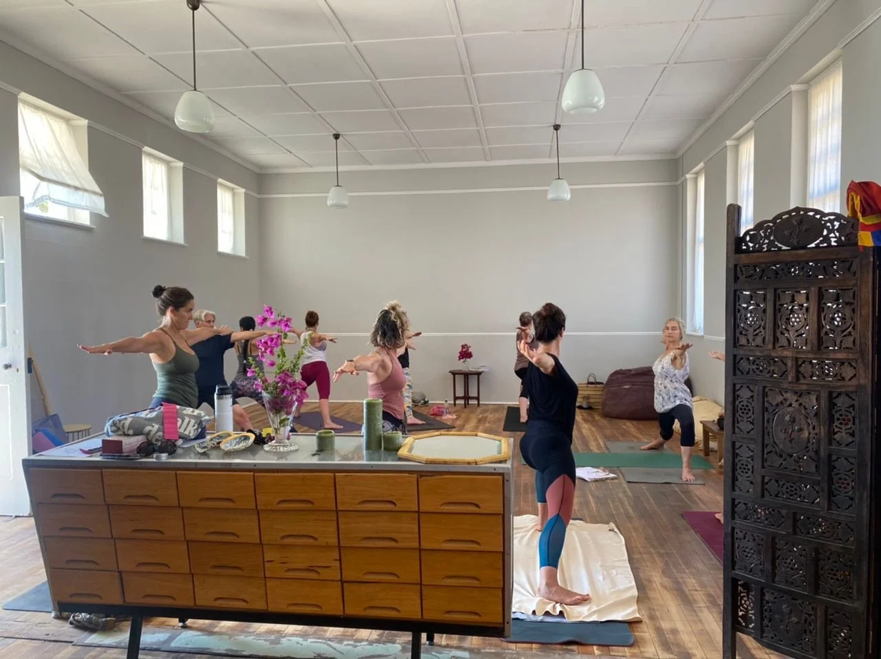 Group of women participating in a yoga class in a bright, spacious room with high ceilings and wooden floors.