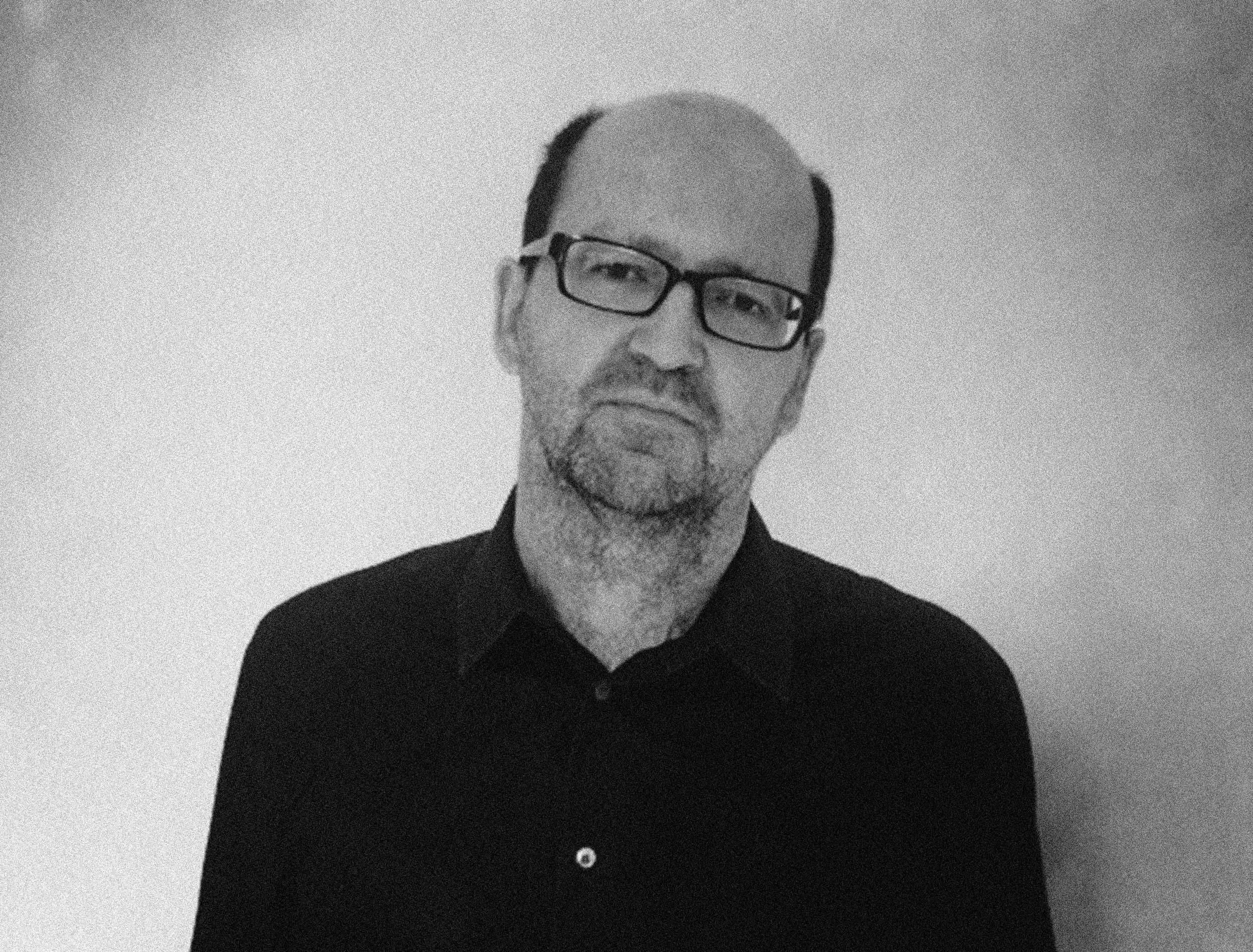 A man with glasses and a beard holding a vintage camera, smiling slightly.