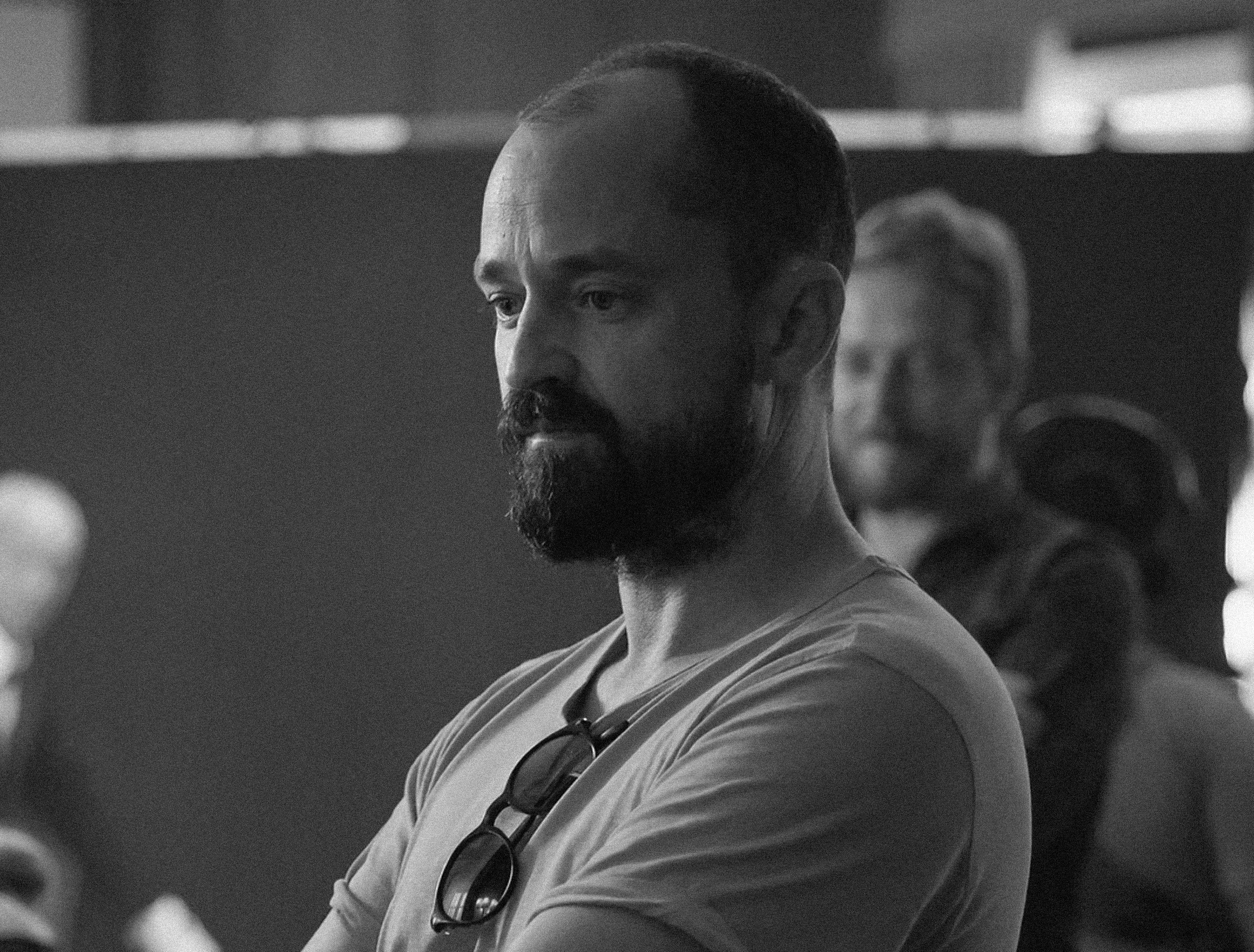 A man with a beard and mustache wearing a knit cap, looking to the side with a contemplative expression, against a dark background.