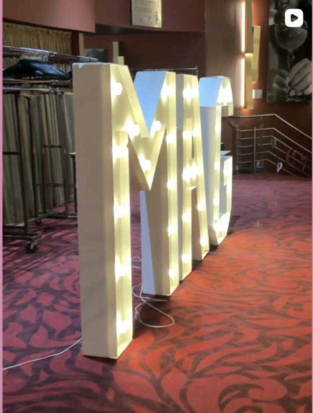 Une grande décoration lumineuse en forme de lettres M et A sur un tapis rouge dans une salle de fête ou événement