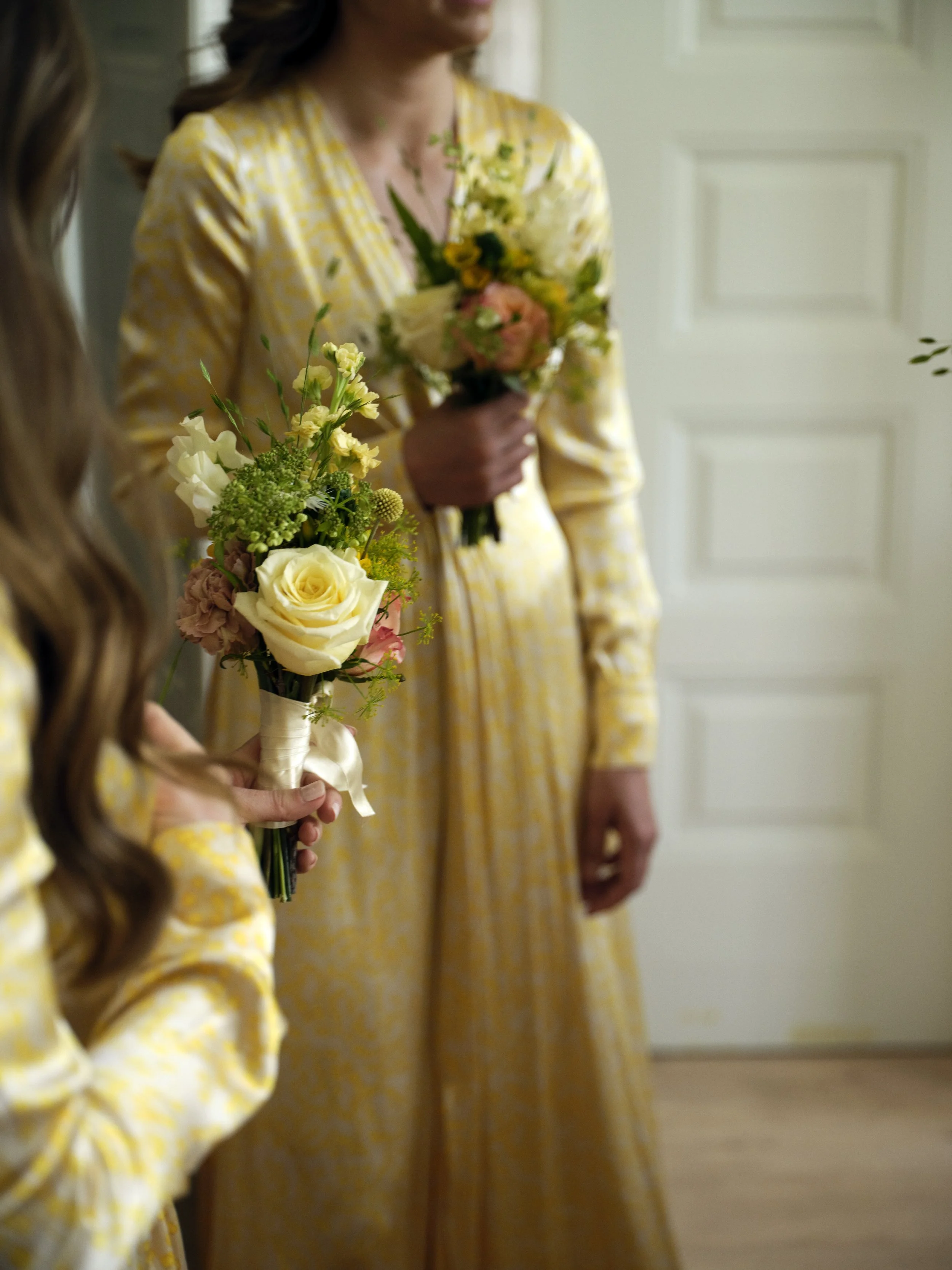 Two women in yellow floral dresses holding bouquets of flowers.