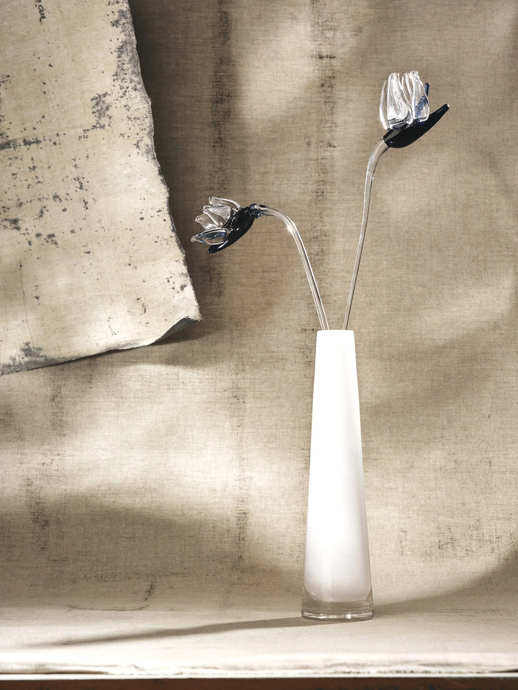 Glass vase with two glass tulip-shaped flowers with dark and clear petals on a beige surface.