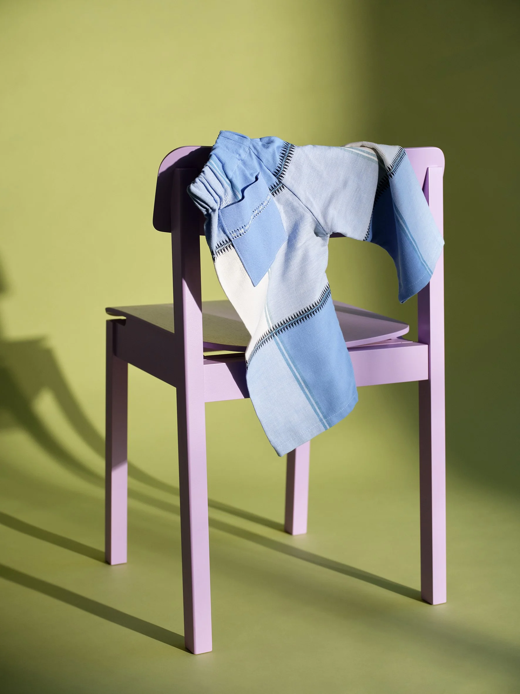 A pink chair with a blue and white striped towel draped over its backrest, set against a yellow background.