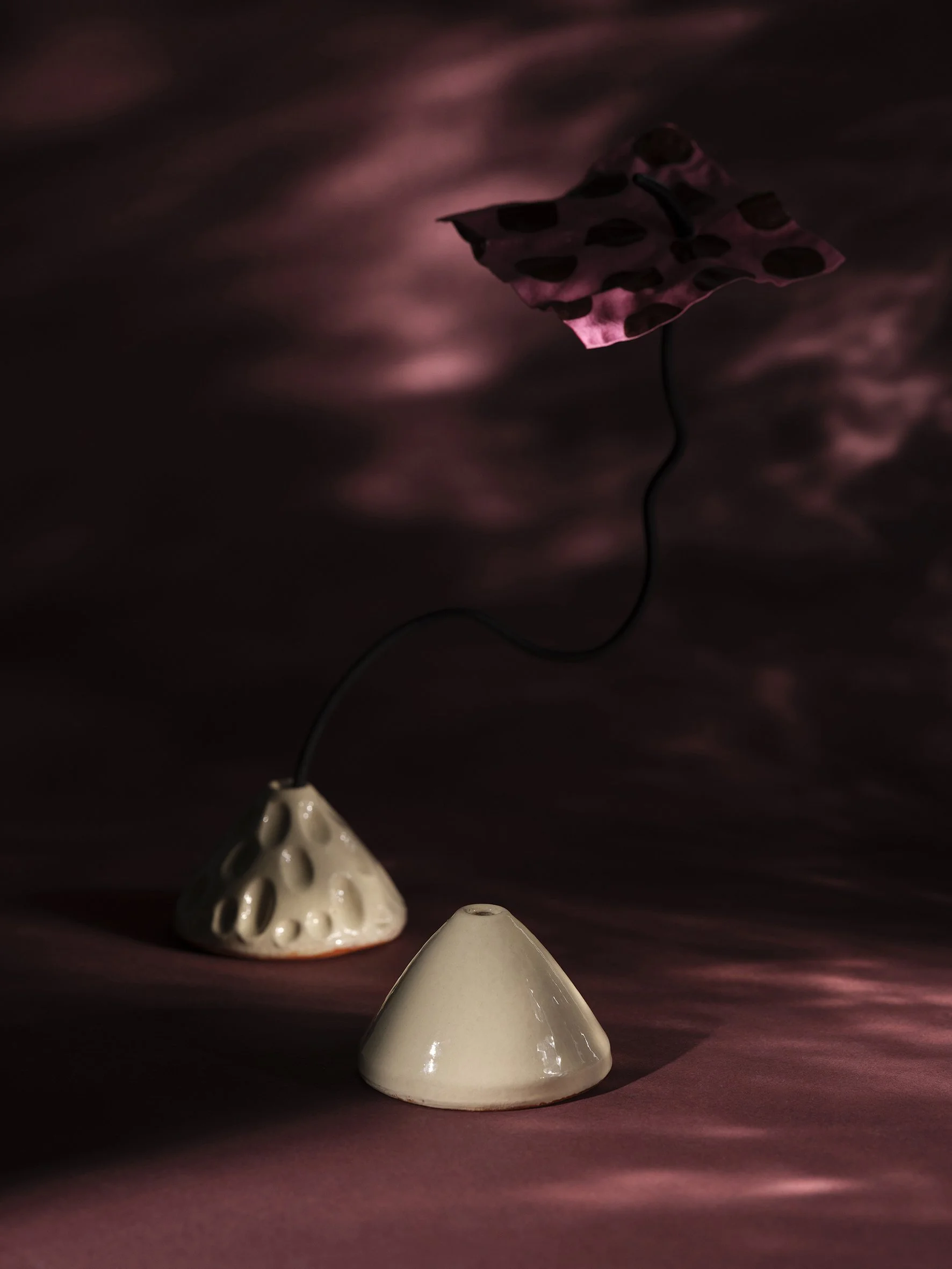 Ceramic cone shaped objects with a polka-dotted paper umbrella connected by a wire, set against a dark, textured background.