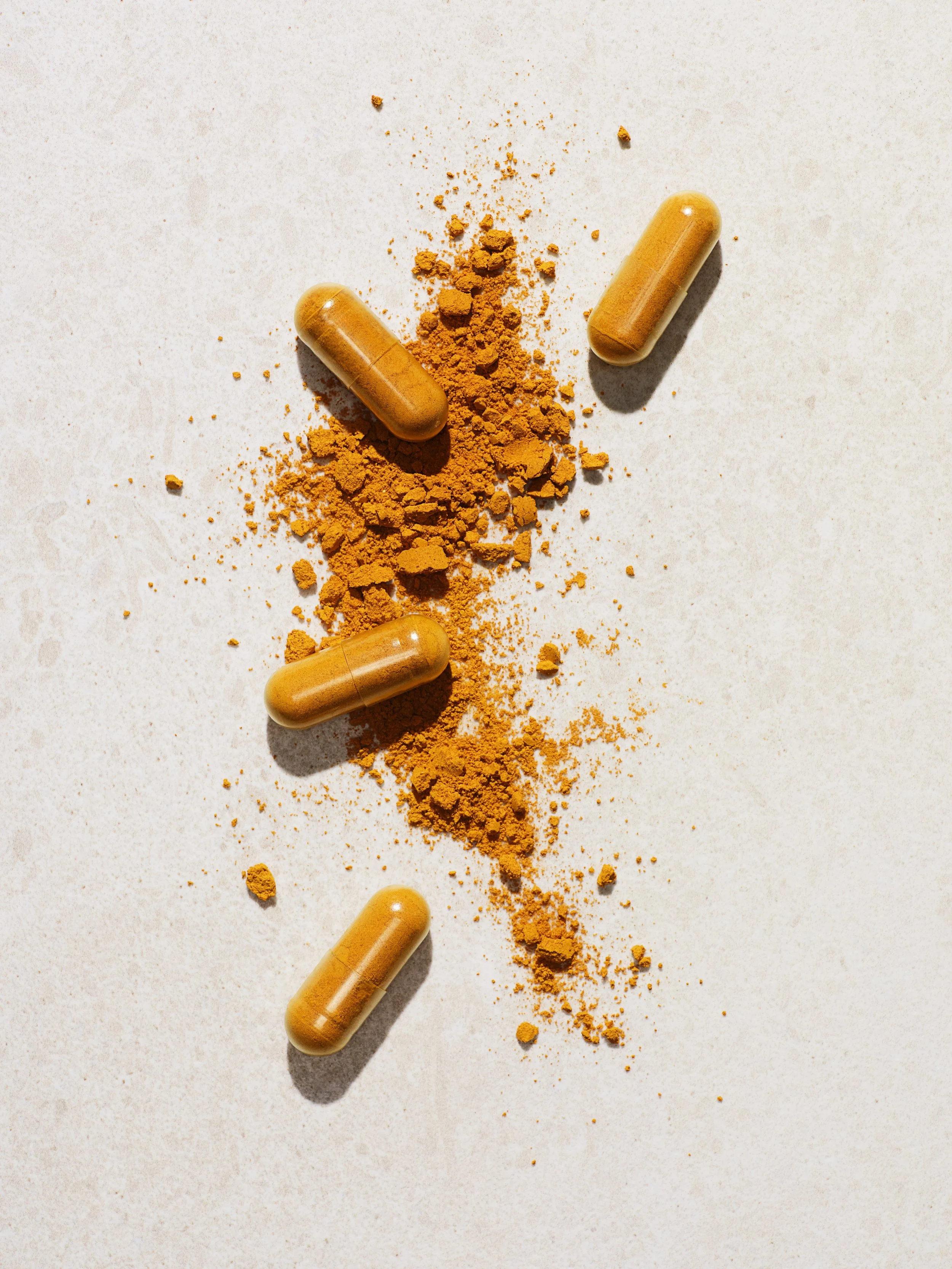 Yellow capsules and orange powder scattered on a light surface.
