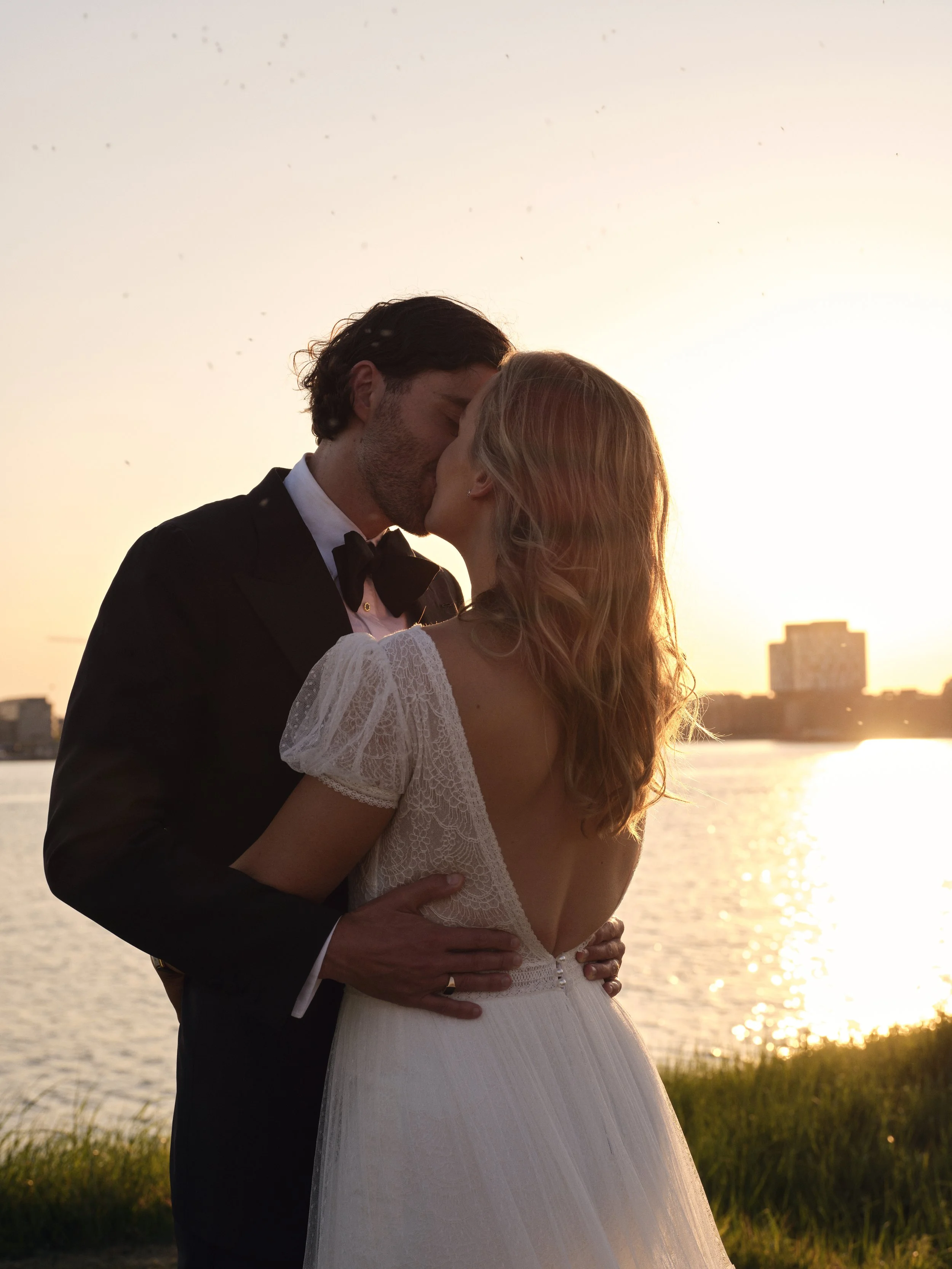 A bride and groom sharing a kiss during sunset by the water.