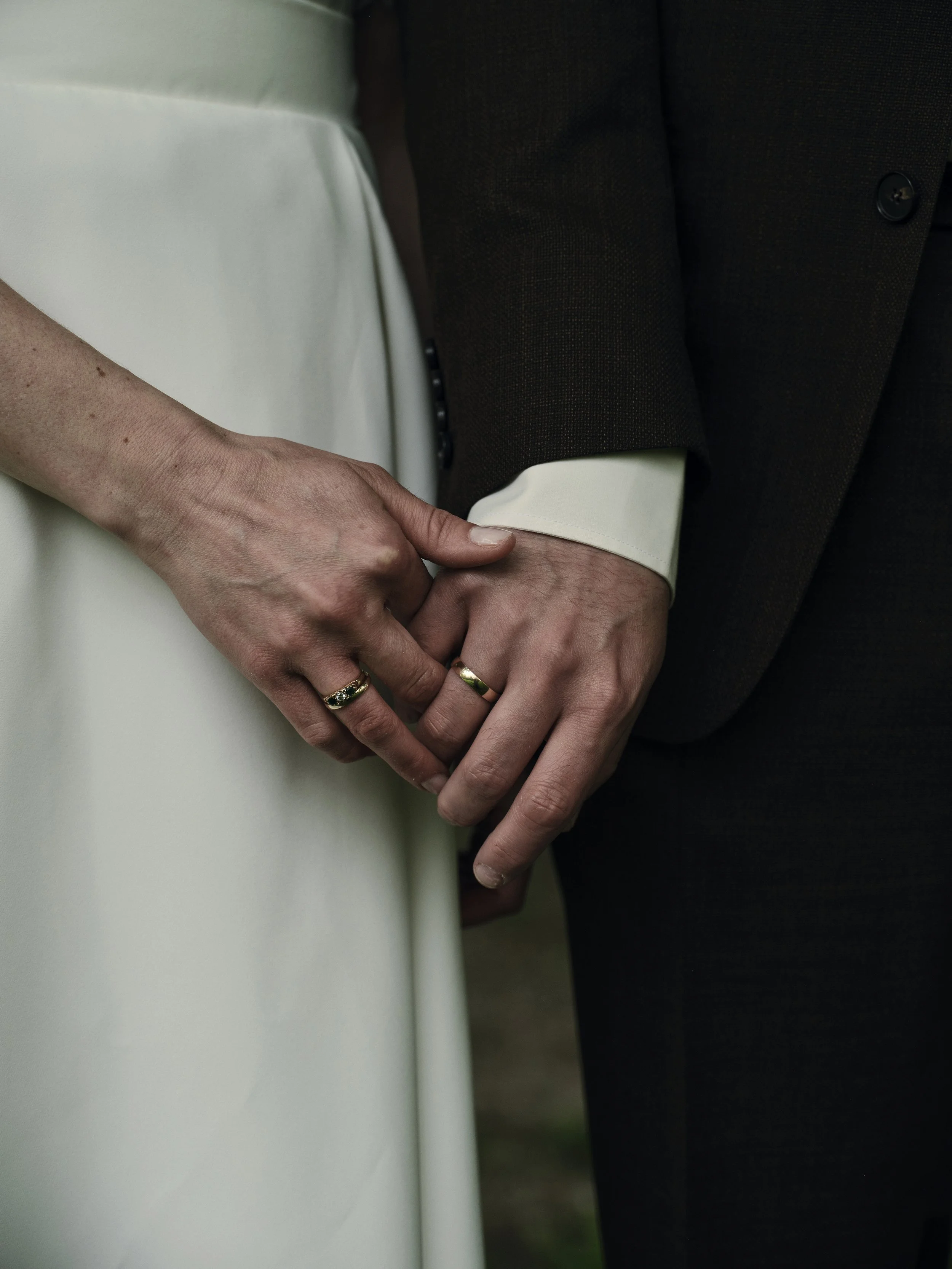 Close-up of a bride and groom holding hands, showing wedding rings on their fingers.
