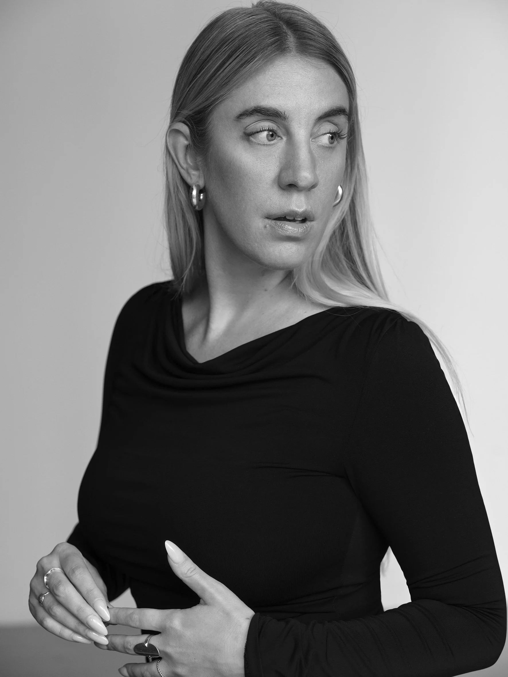 Black and white portrait of a woman with blonde hair, wearing a black top and hoop earrings, looking to her left.
