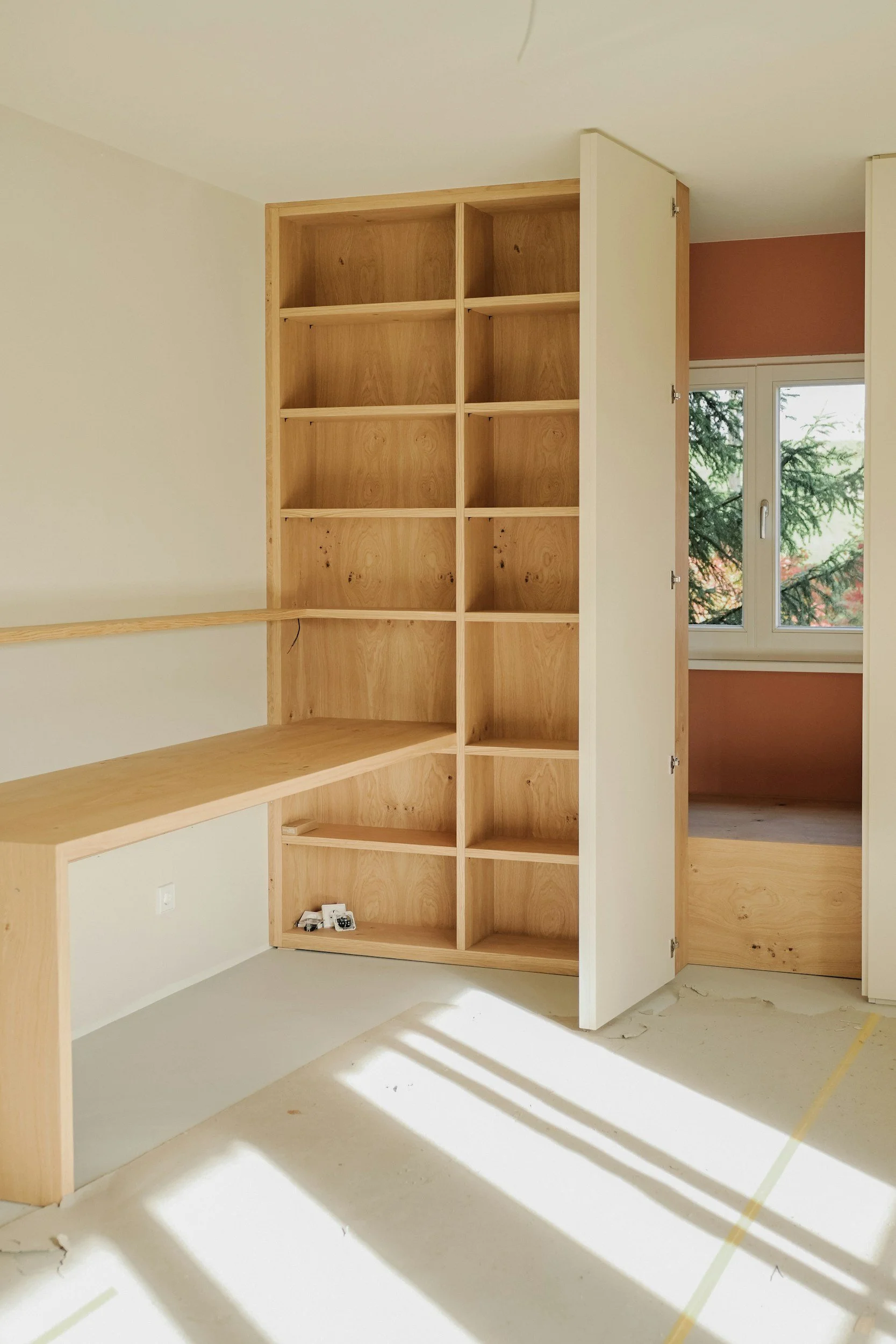 Empty wooden shelving unit and desk in a room with a window and sunlight.
