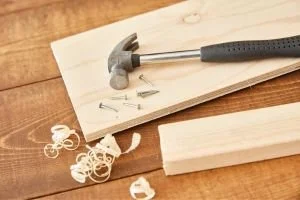 Hammer, nails, and wood on a wooden surface, possibly for building or woodworking.