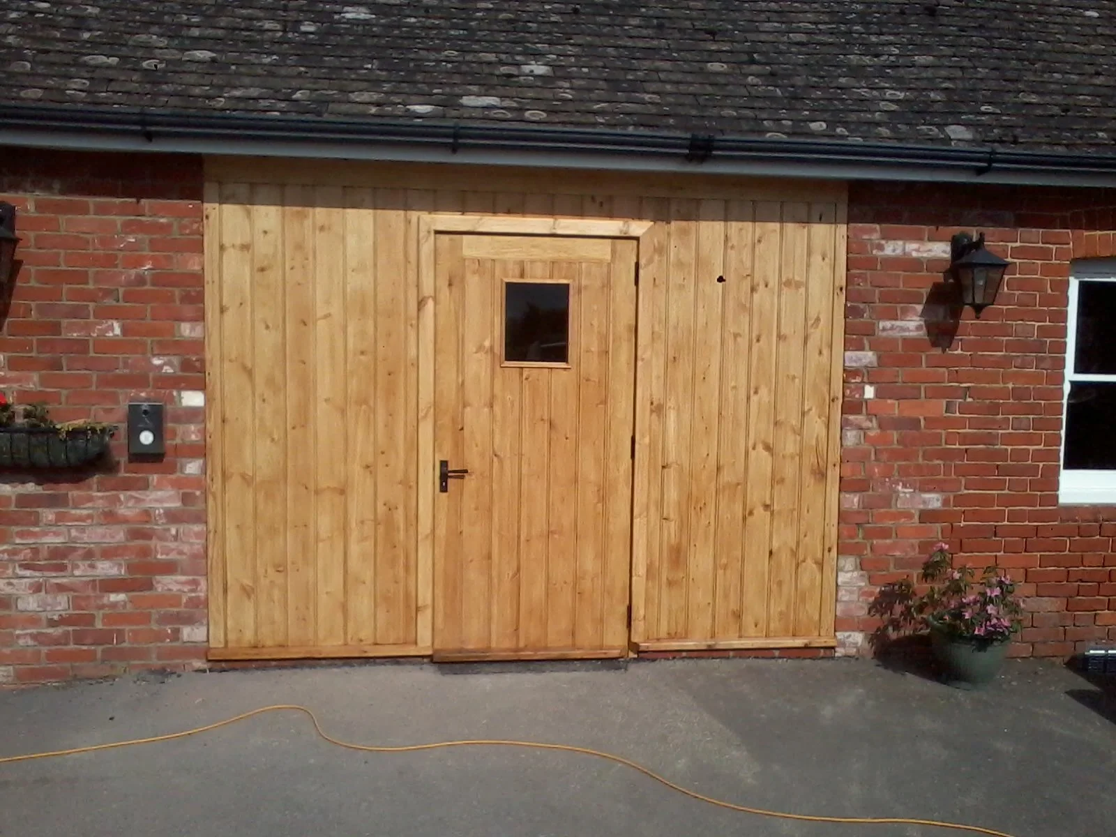 A newly installed wooden door with a small square window in a brick house exterior. Hampshire and Surrey