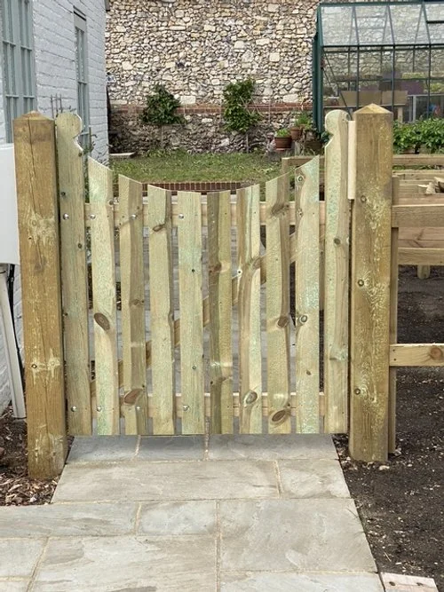 A newly built wooden garden gate with vertical planks, flanked by four sturdy wooden posts,