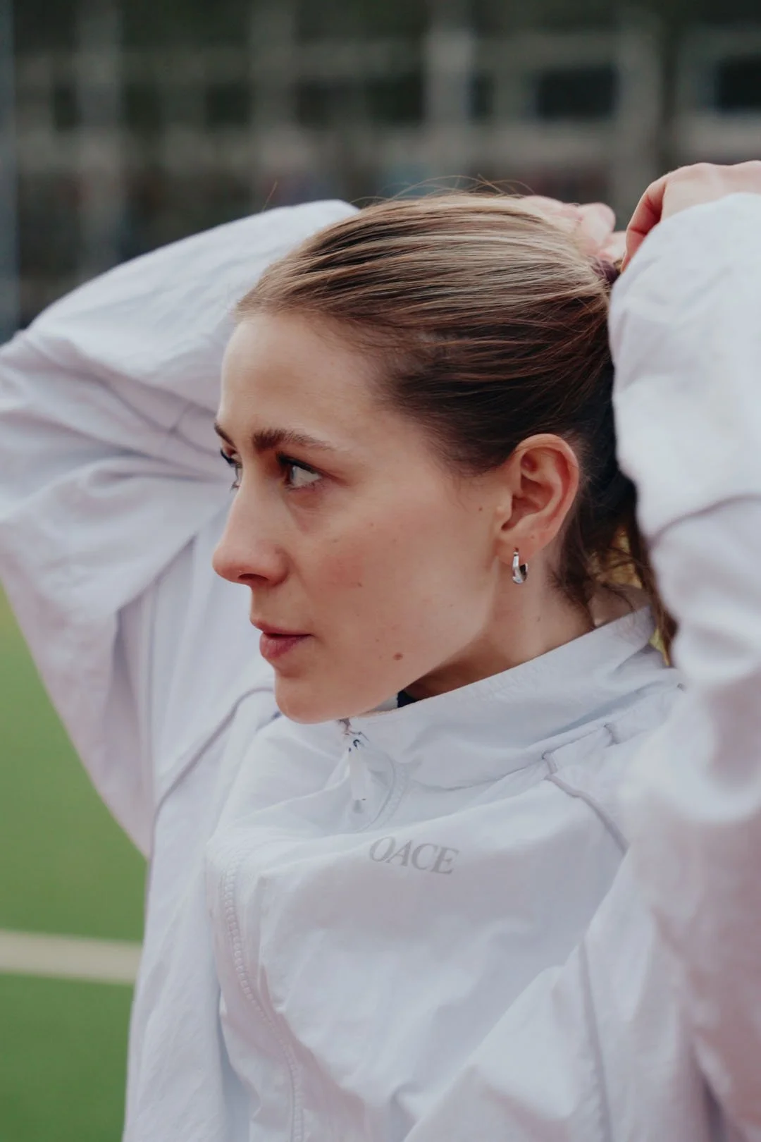 portraitfoto von hanna rabisch wie sie sich grade die haare zu einem zopf bindet. sie trägt eine weiße trainingsjacke der marke oace.