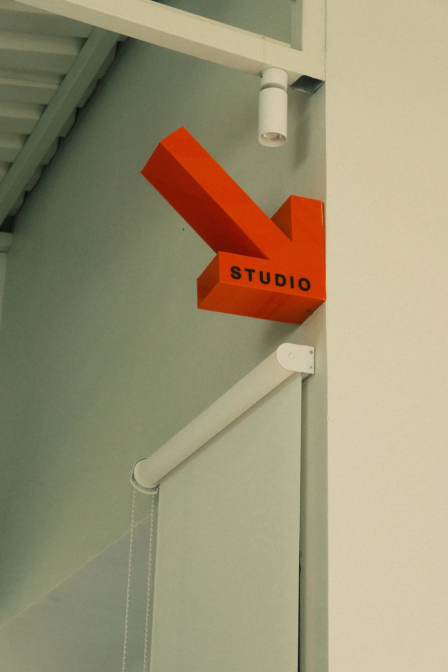 Inside the Supercool Studio Bali. Orange sign with the word 'STUDIO' and a large arrow pointing to the right, mounted on a wall near the ceiling.