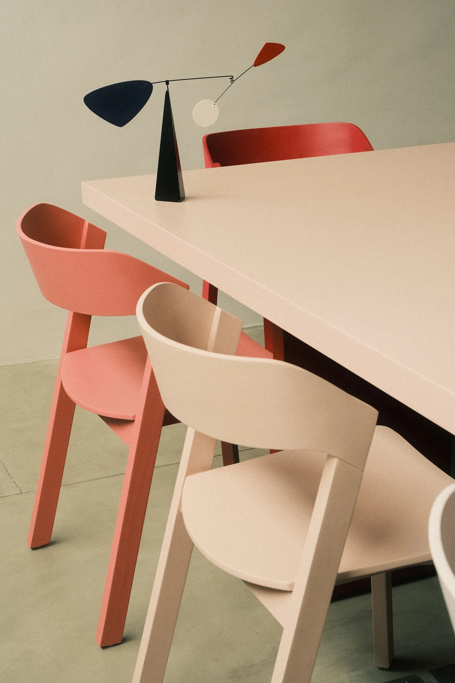 Inside the Supercool Studio Bali. A modern dining table with four pastel-colored chairs and a unique metal table lamp with an abstract design.