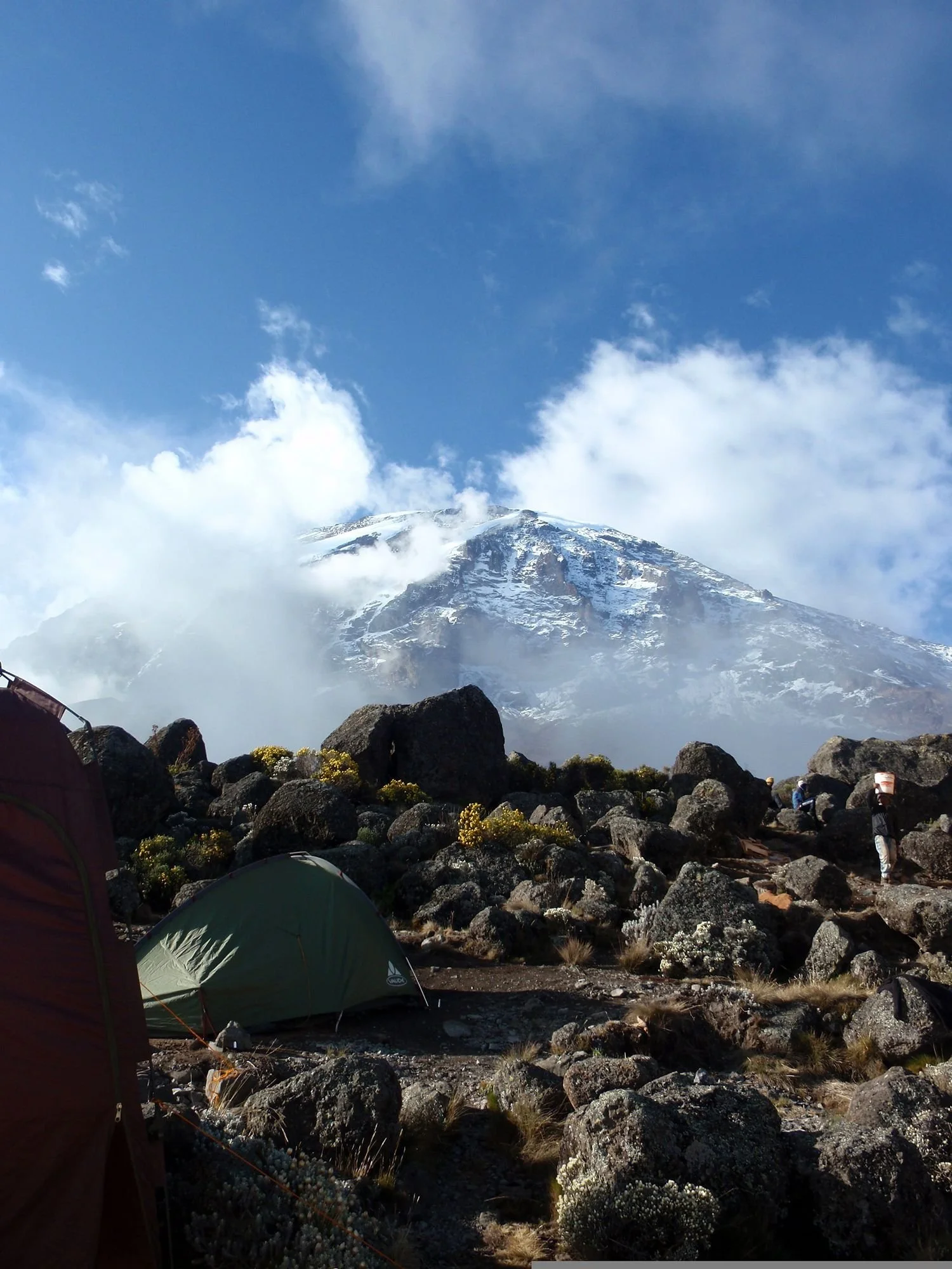 Tent op een rotsachtige vlakte voor een besneeuwde bergtop, tijdens de beklimming van de Kilimanjaro in Tanzania.