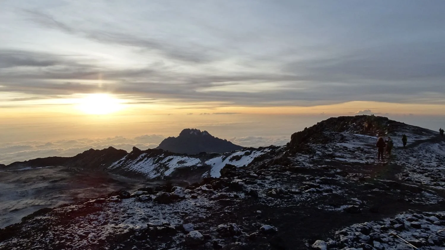 Zonsopgang boven een rotsachtige berg met hier en daar sneeuw, tijdens de beklimming van de Kilimanjaro.