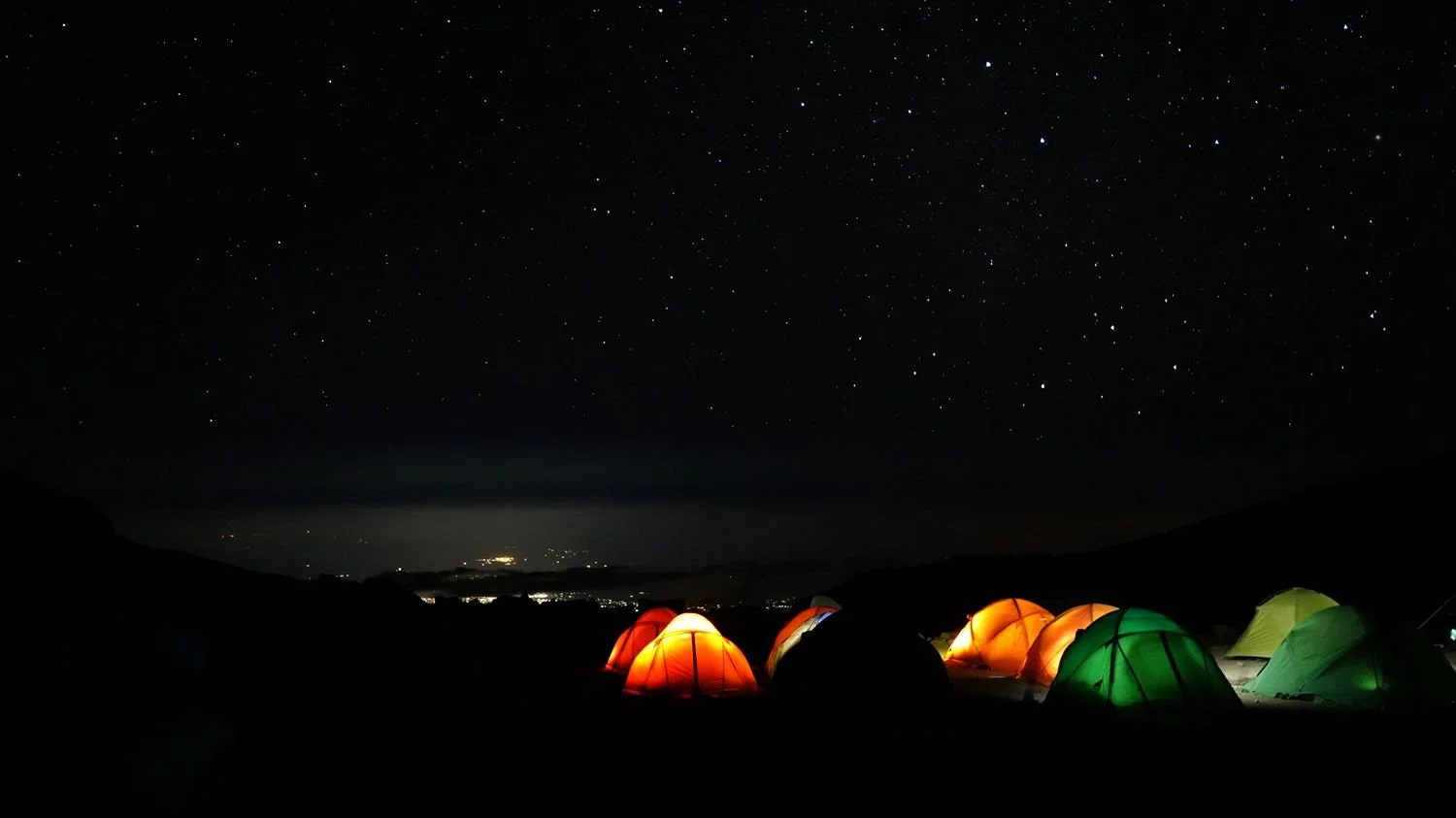 Tien kleurrijke tenten op een camping onder een heldere, sterrijke nachtelijke hemel.
