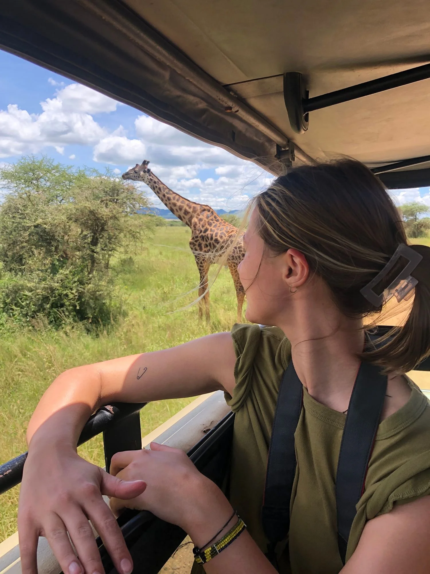 Een vrouw kijkt uit een safarivoertuig naar een giraffe die blaadjes aan het eten is van een boom, tijdens een safari in Tanzania.
