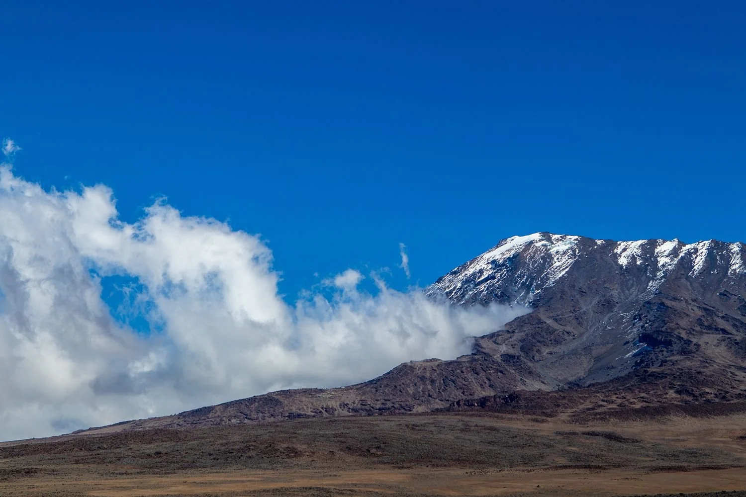 Wolken naast een besneeuwde bergtop bij de beklimming van de Kilimanjaro.