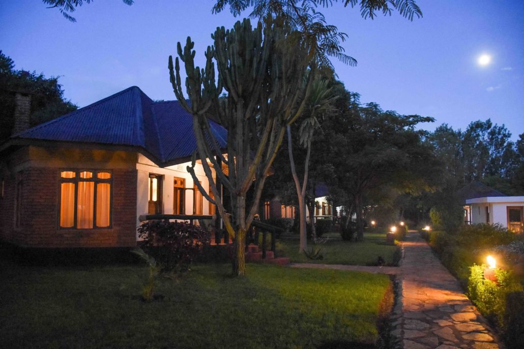 Een tuin met een kavelhuis en een met lampjes verlichte pad, 's avonds met de maan aan de hemel.
