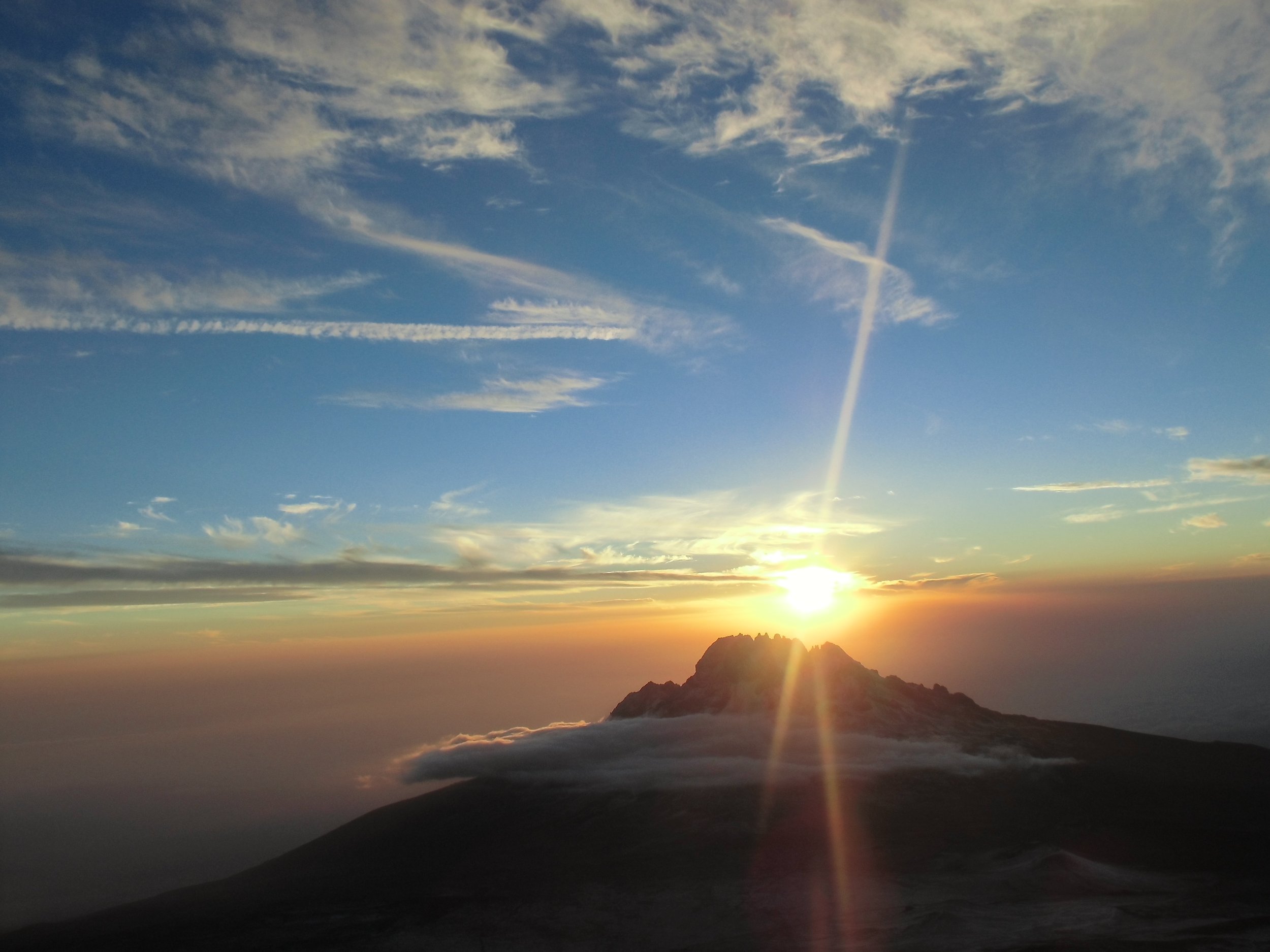 Zonsopgang boven een bergtop, met de zon die net boven de horizon uitkomt en wolken die verlicht worden door het zonlicht.