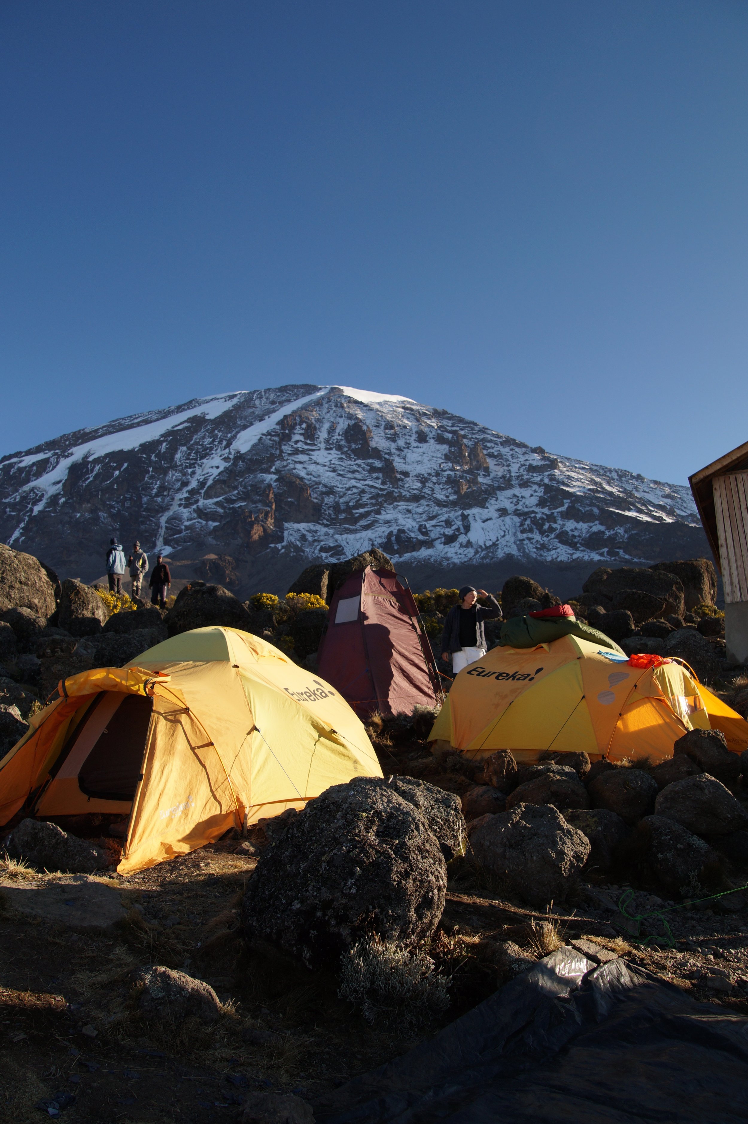 Tentenkamp op een rotsachtig terrein met een berg met besneeuwde top op de achtergrond.