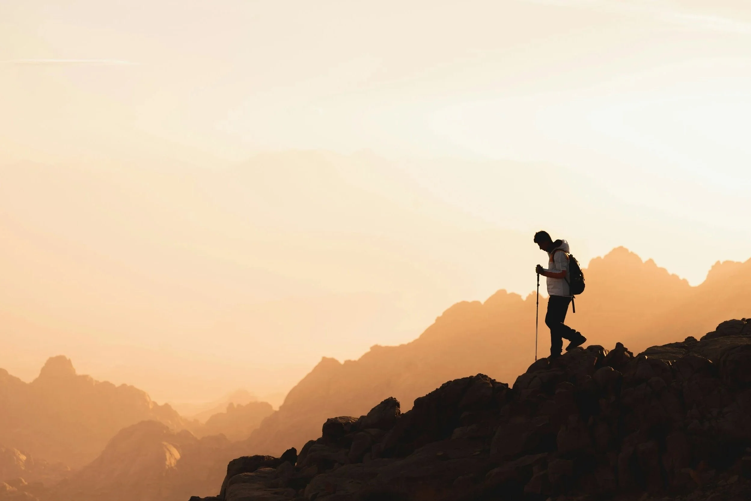 Silhouet van een persoon met een wandelstok op een rotsachtig bergpad bij zonsondergang, bij de beklimming van de Kilimanjaro in Tanzania.
