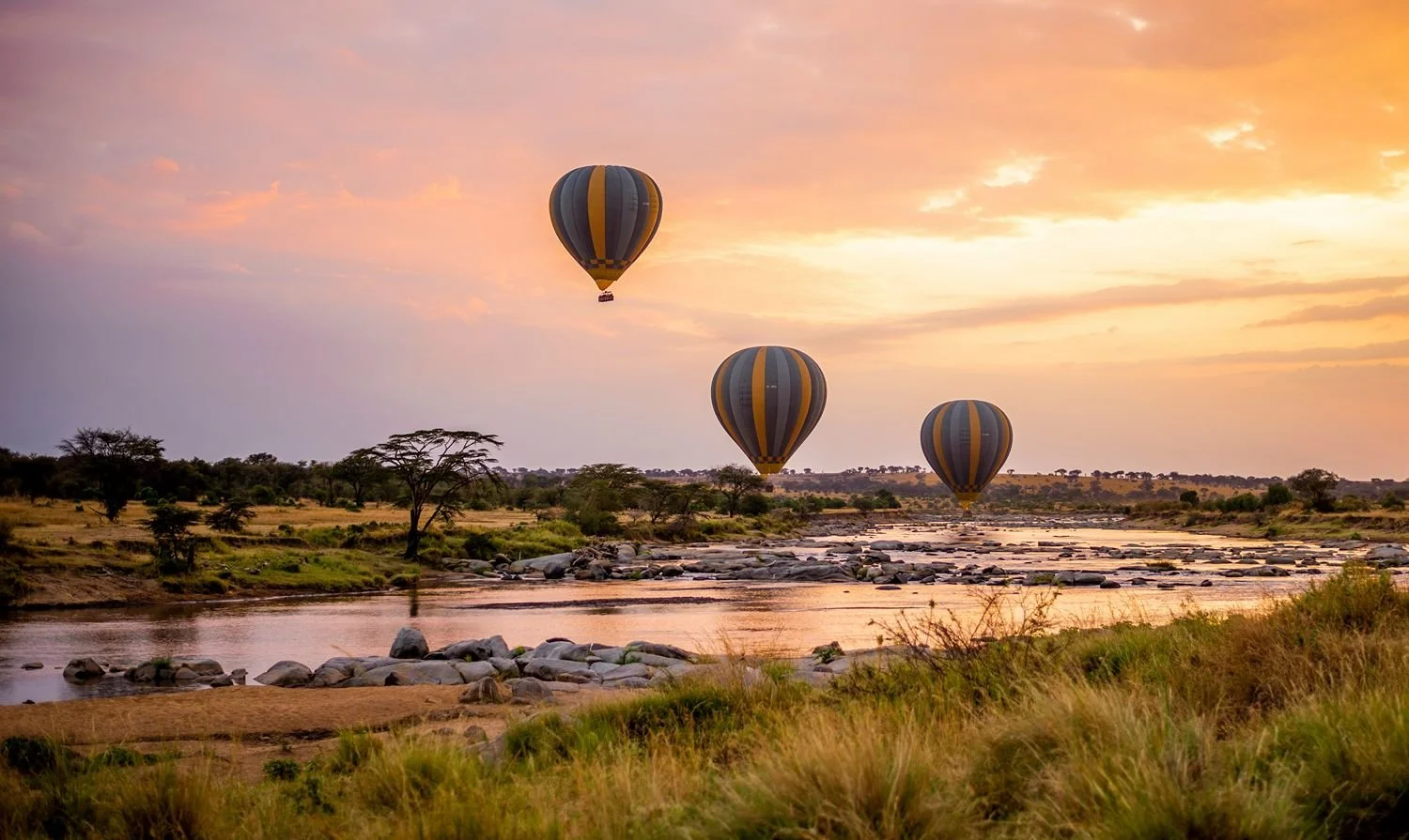 Drie ballonnen boven een vijver op de Serengeti bij zonsopgang, tijdens een safari in Tanzania.