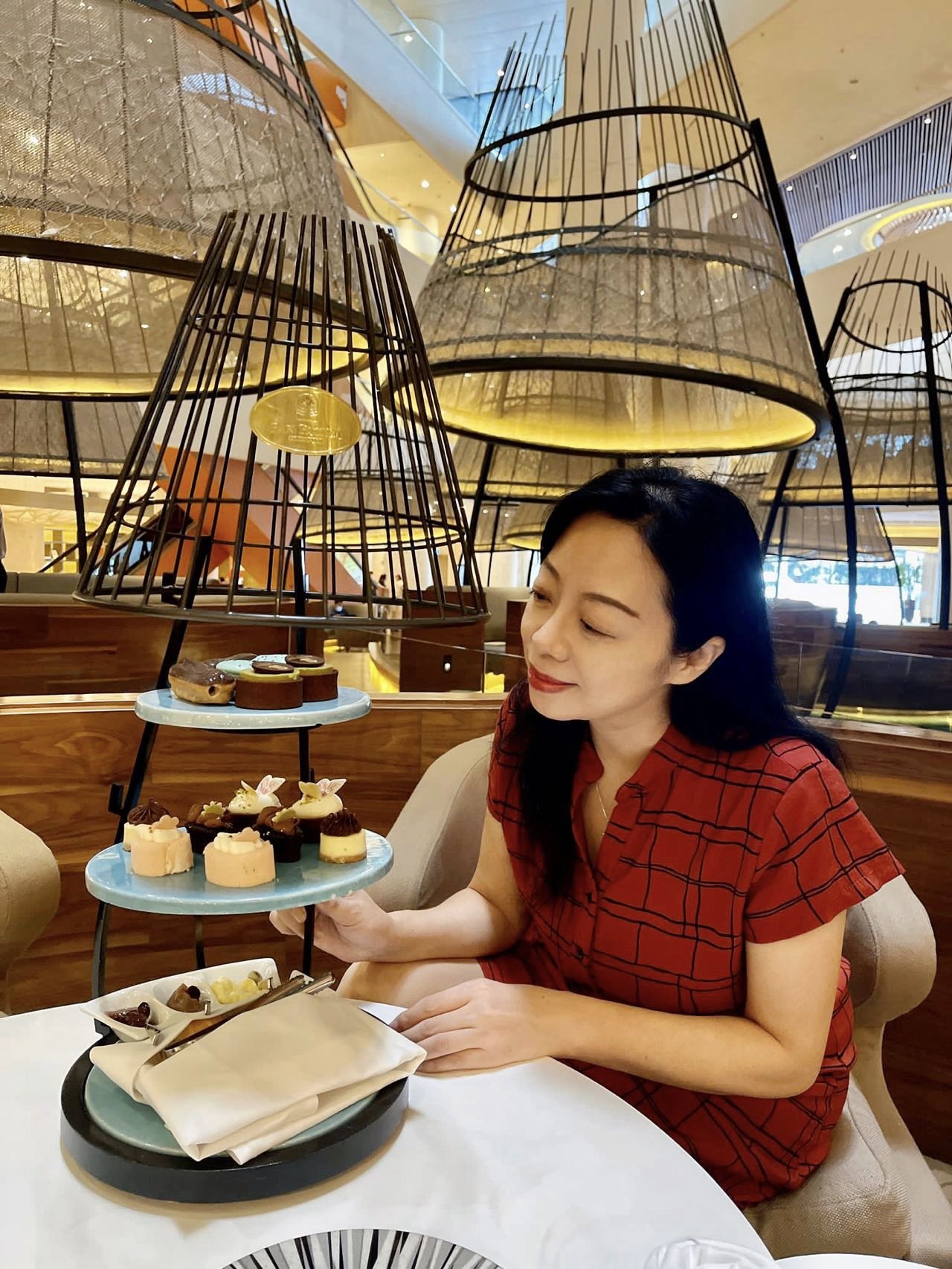 Woman in red dress enjoying a dessert at a restaurant with a three-tiered serving stand of assorted desserts.
