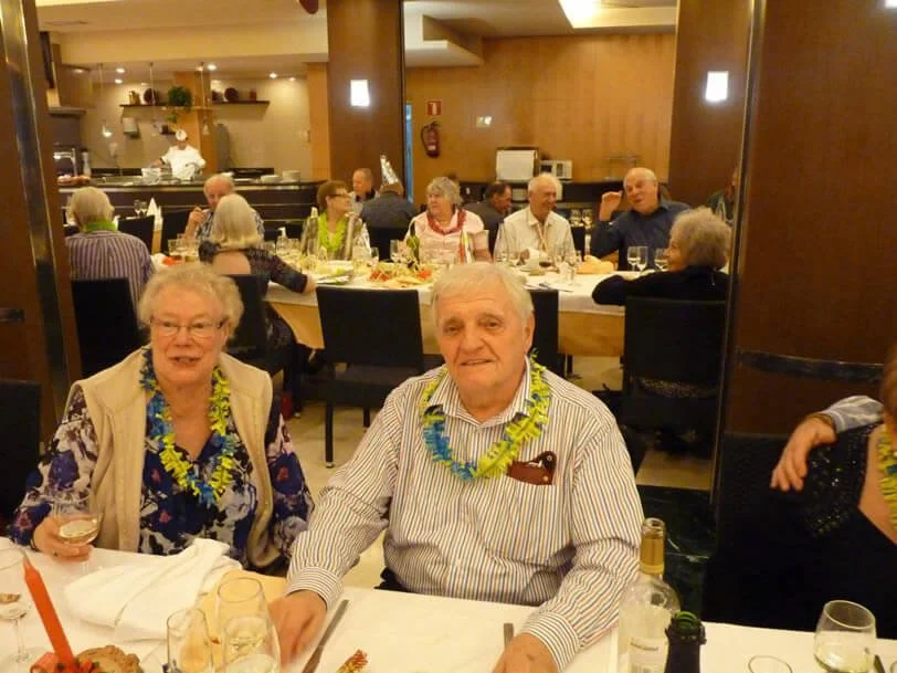 Group of elderly people at a festive dinner party, wearing leis, in a warmly decorated restaurant.