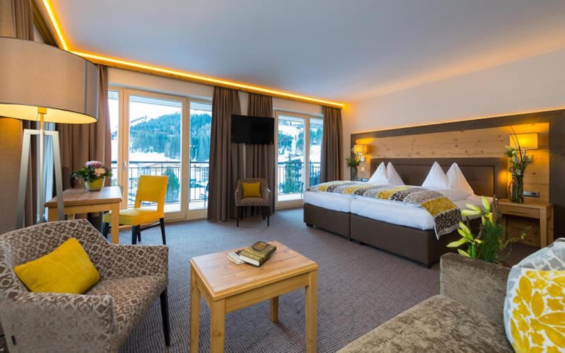 Hotel room with a large bed, seating area, TV, and balcony with mountain view.