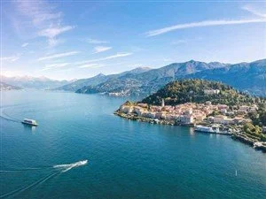 Aerial view of a large lake with boats, surrounded by mountainous landscape and a small town on the shoreline.