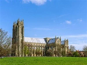 A historic cathedral with tall spires and Gothic architecture, set against a blue sky with some clouds, surrounded by a grassy area.