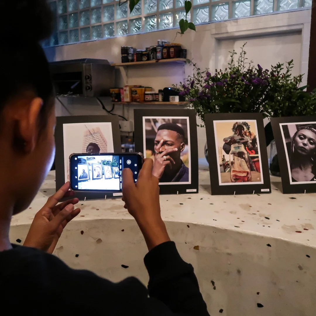 Person taking a photo of framed portraits displayed on a counter, with a plant and shelves in the background.