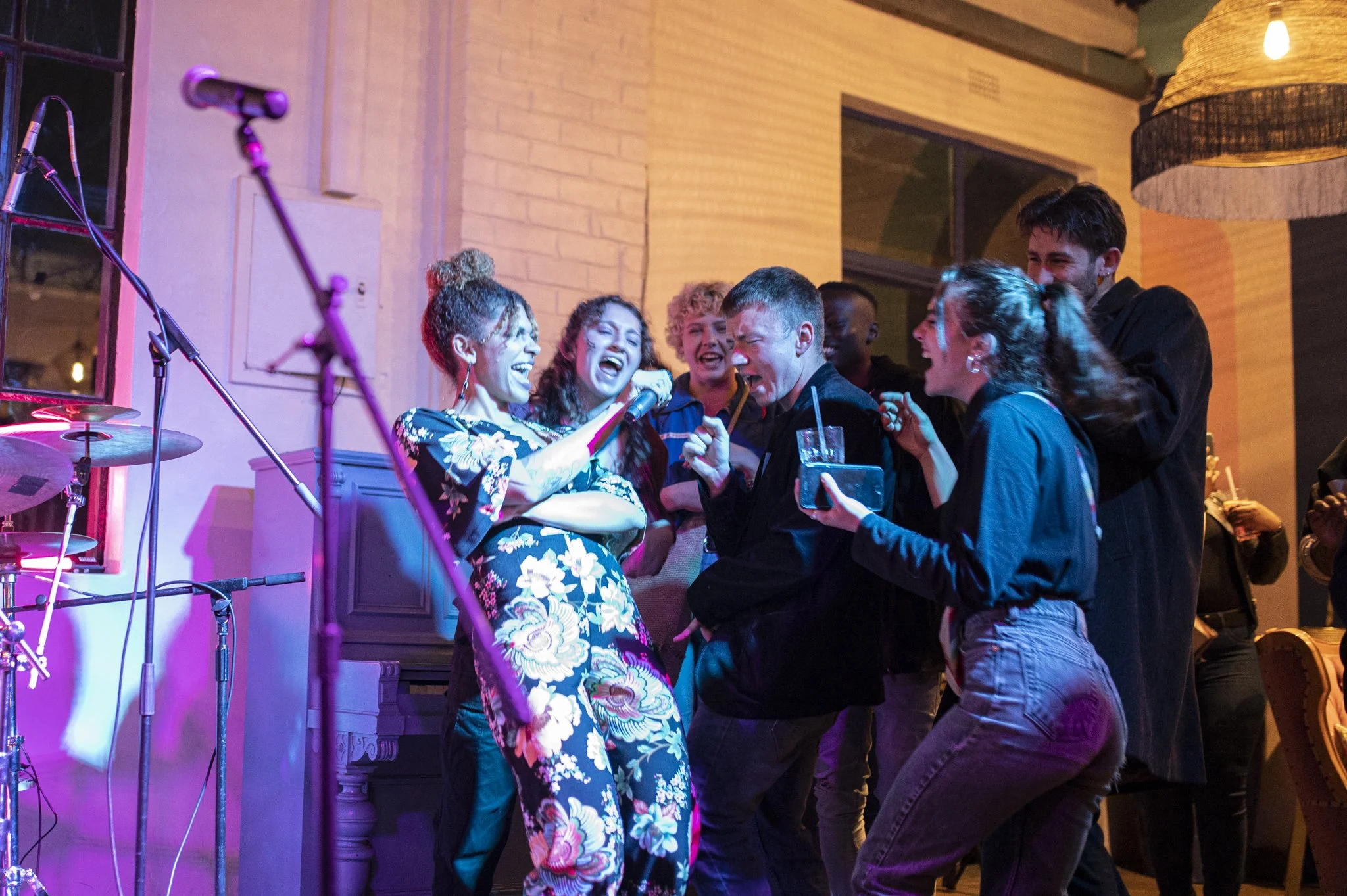 Group of people singing, dancing, and enjoying a lively moment at a party with musical instruments nearby.