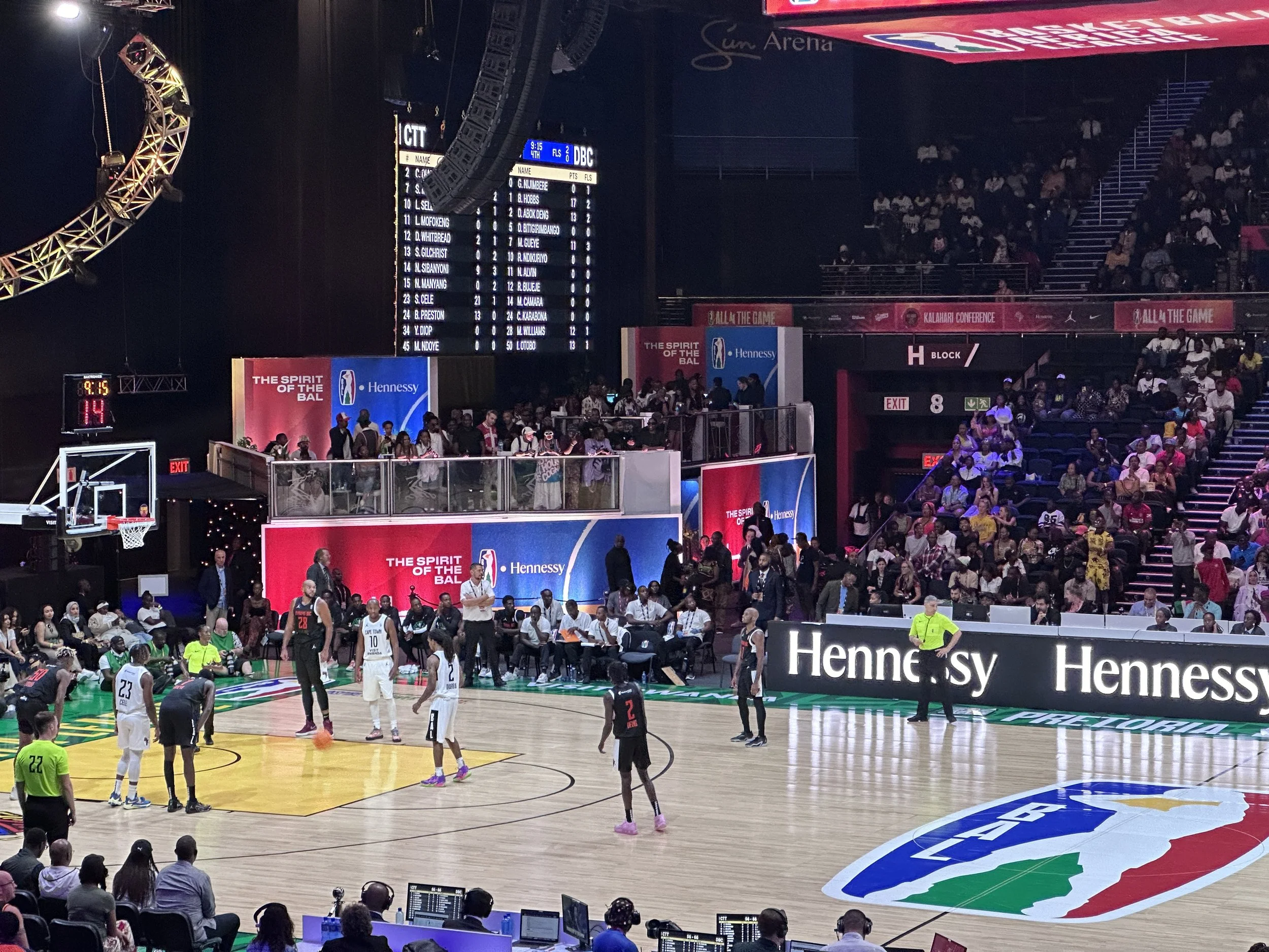 Basketball game inside the arena with players, referees, and spectators watching from the stands.
