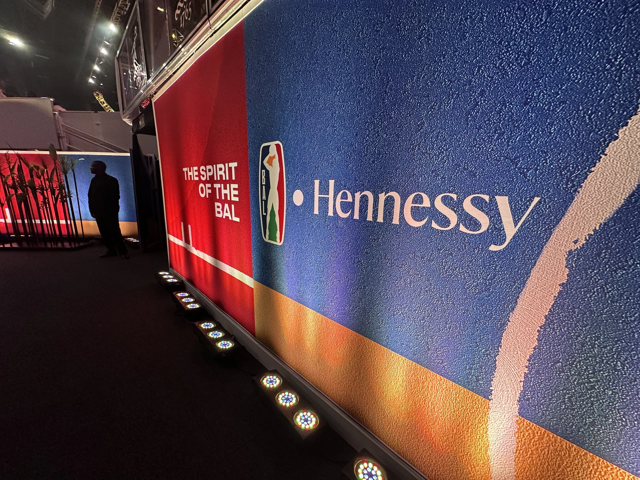 A colorful NBA-themed display with the slogan "The Spirit of the Ball" and branding for Hennessy, featuring a silhouette of a person and a fence in the background.