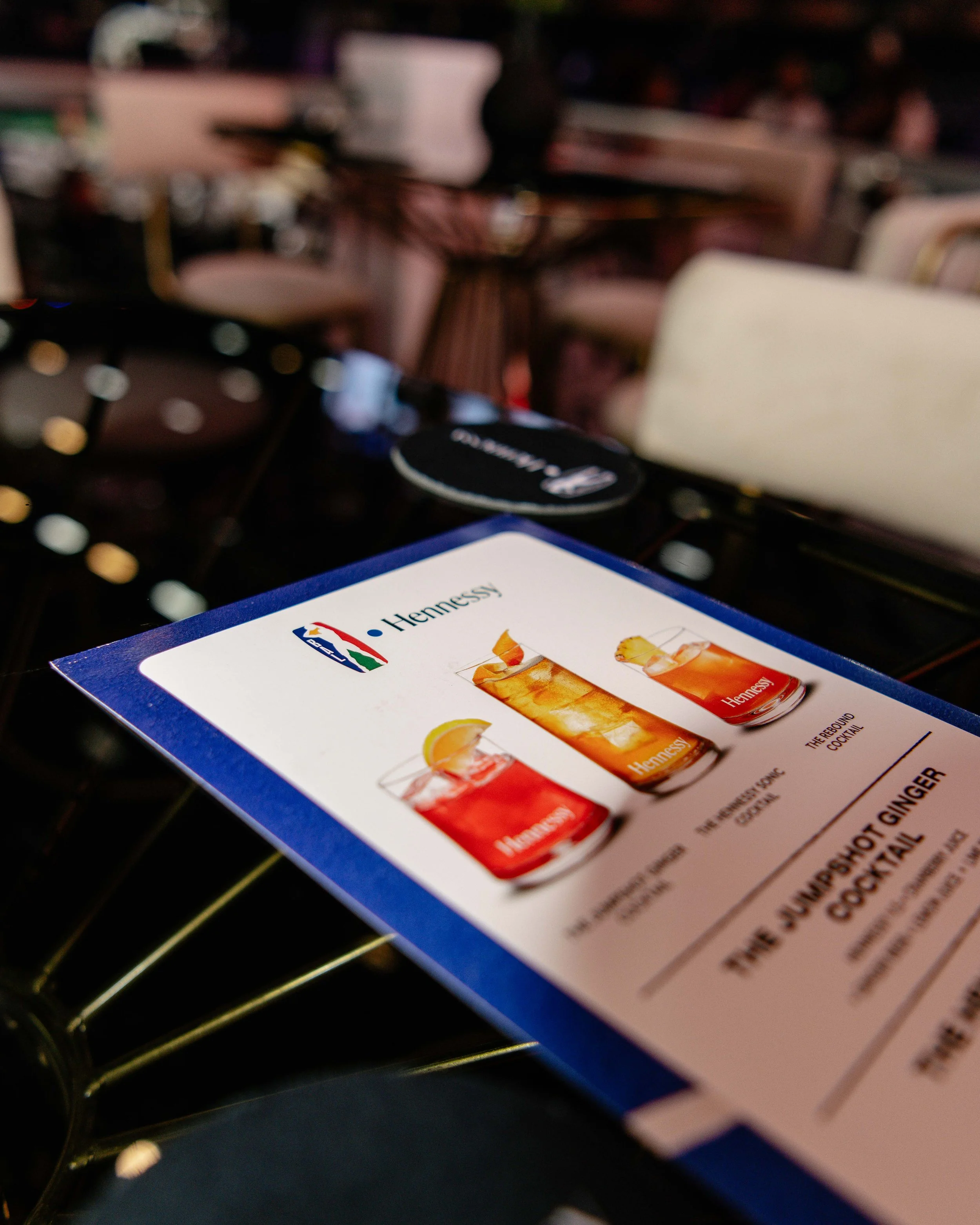 Close-up of a Hennessy cocktail menu featuring three drinks with different garnishes, placed on a table in a dimly lit restaurant or bar setting.