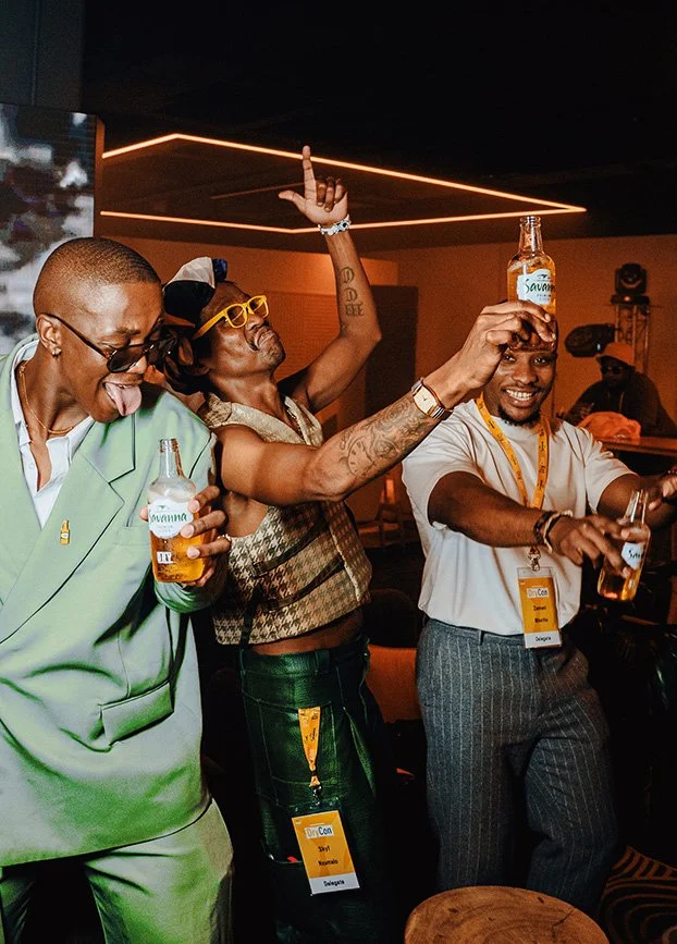 Three men at a party enjoying drinks, one of them balancing a beer bottle on his head.